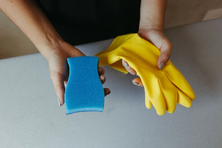 Homme anonyme portant des gants en latex jaunes et un t-shirt foncé, essuyant le miroir de la salle de bain avec une serviette en papier
